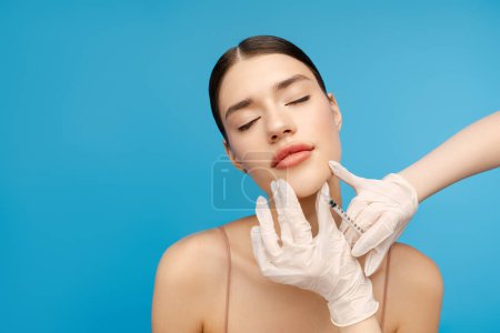 Photo for Pretty woman closing her eyes while getting anti aging injection. Copy space. Isolated on blue background. Beauty care, anti aging procedures, plastic surgery concept - Royalty Free Image