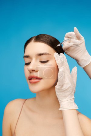 Photo for Pretty young woman getting anti aging injection on her face to reduce wrinkles. Isolated on blue background. Beauty care, anti aging procedures, plastic surgery concept - Royalty Free Image