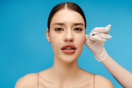 Photo for Beautiful young woman receiving hyaluronic acid injection by beautician. Isolated on blue background. Beauty care, anti aging procedures, plastic surgery concept - Royalty Free Image