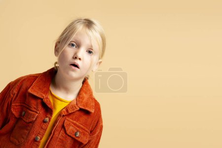 Téléchargez les photos : Portrait d'une jolie petite fille mignonne excitée à bouche ouverte regardant la caméra isolée sur fond beige espace de copie. Concept de publicité - en image libre de droit