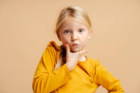 Téléchargez les photos : Portrait de mignonne petite fille de mode portant des vêtements décontractés mannequin posant debout isolé sur fond beige. Concept de publicité - en image libre de droit