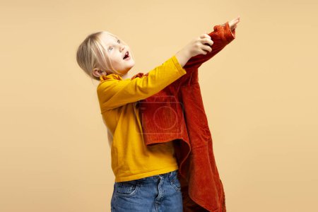 Téléchargez les photos : Jolie petite fille concentrée portant une veste brune tout en préparant aller à l'école à fond beige. Concept d'enfance - en image libre de droit