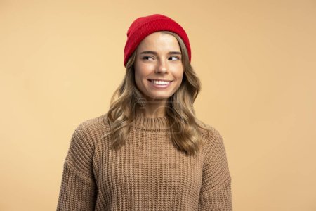 Photo for Portrait of young smiling woman wearing red hipster hat and stylish winter sweater looking away isolated on beige background. Fashion, natural beauty concept - Royalty Free Image