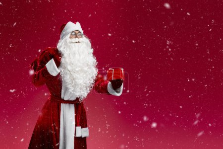 Téléchargez les photos : Père Noël tenant le sac, transporter des cadeaux isolés sur fond rouge, espace de copie. Vacances, Noël, concept publicitaire - en image libre de droit