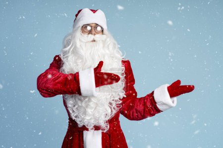 Foto de Divertido San Nicolás o Santa Claus señalando con las manos sobre fondo azul, nieve. Concepto vacaciones de invierno - Imagen libre de derechos