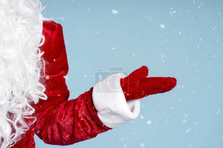 Téléchargez les photos : Grosse main du Père Noël montrant de la neige isolée sur fond bleu, de la neige. Concept vacances d'hiver - en image libre de droit
