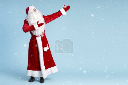 Foto de Santa Claus mostrando las manos sobre nieve aislada sobre fondo azul. Concepto vacaciones de invierno - Imagen libre de derechos