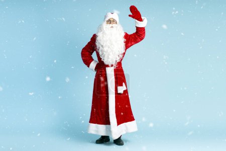 Foto de Saludo de Papá Noel, mano agitada aislada sobre fondo azul con nieve, espacio para copiar. Vacaciones de invierno, Navidad, concepto de publicidad - Imagen libre de derechos