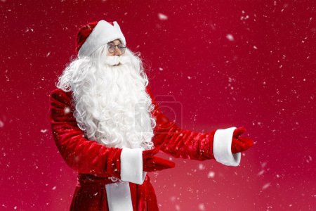 Téléchargez les photos : Père Noël pointant les mains sur la neige isolée sur fond bleu. Concept du temps de Noël - en image libre de droit
