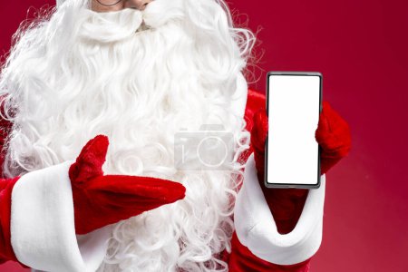 Photo for Closeup of Santa hand holding mobile phone showing screen isolated on red background, mockup. Online shopping, sale, mobile app concept - Royalty Free Image
