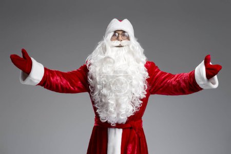 Téléchargez les photos : Drôle Père Noël tenant les mains grandes ouvertes, étreignant en regardant la caméra isolée sur fond gris. Concept de vacances - en image libre de droit