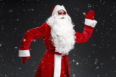 Téléchargez les photos : Homme émotionnel drôle portant costume du Père Noël, lunettes de danse, s'amuser sur la fête du Nouvel An isolé sur fond noir - en image libre de droit