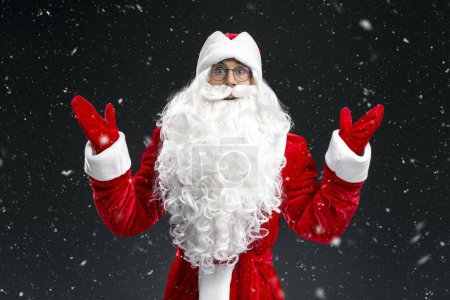 Foto de Retrato de divertido Papá Noel emocional cogido de la mano aislado sobre fondo negro con nieve. Concepto vacaciones de invierno - Imagen libre de derechos