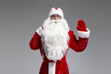 Foto de Santa Claus bolsa de mano con regalos saludo, saludando mano aislada sobre fondo gris. Vacaciones de invierno, Navidad, concepto de publicidad - Imagen libre de derechos