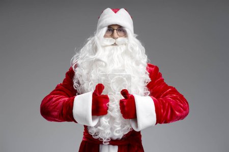 Photo for Portrait of Santa Claus holding thumbs up looking at camera isolated on gray background. Happy New Year, Christmas, holiday, winter concept - Royalty Free Image