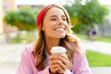 Téléchargez les photos : Femme attrayante souriante portant chapeau rouge tenant tasse de café regardant loin assis dans le café. Style de vie positif, concept de pause café - en image libre de droit