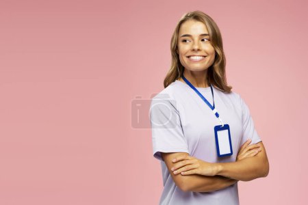 Foto de Hermosa mujer joven sonriente, vendedor consultor con camiseta y placa en blanco mirando hacia otro lado aislado sobre fondo rosa, espacio de copia. Tarjeta de nombre, Mockup - Imagen libre de derechos