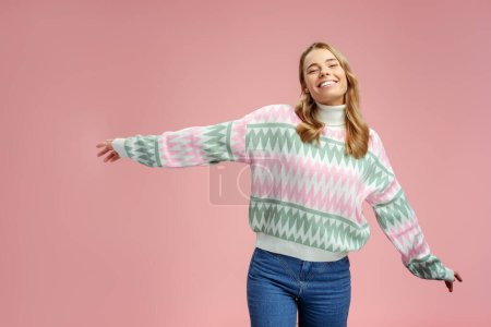 Foto de Mujer rubia sonriente con suéter de invierno con estilo, vaqueros bailando aislados sobre fondo rosa, espacio para copiar. Atractiva modelo de moda feliz posando para imágenes en el estudio. Compras, tienda, concepto de venta - Imagen libre de derechos