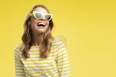 Photo for Portrait happy beautiful woman with stylish hair wearing sunglass looking away isolated on yellow background, copy space. Fashion model posing for pictures in studio. Advertisement, summer, travel - Royalty Free Image