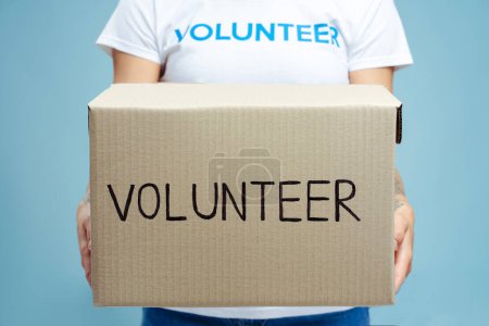 Photo for Closeup woman hands holding carton volunteer box with donations isolated on blue background, selective focus. Charity center, help, social concept - Royalty Free Image
