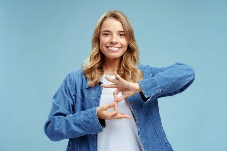 Photo for Smiling confident sign language interpreter or teacher communicating by hands gestures isolated on blue background. Nonverbal communication concept - Royalty Free Image