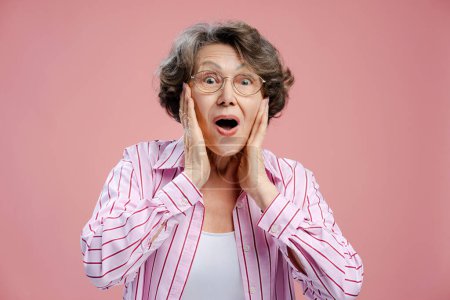 Foto de Retrato de mujer de pelo gris excitado atractivo positivo con peinado elegante con gafas de vista camisa rosa mirando a la cámara aislada en el fondo rosa. Concepto de compras, publicidad - Imagen libre de derechos