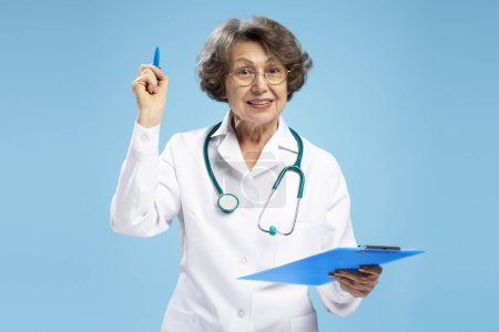 Téléchargez les photos : Portrait de femme âgée aux cheveux gris, médecin tenant le diagnostic, écriture recette debout isolé sur fond bleu. Concept de médecine, soins de santé - en image libre de droit
