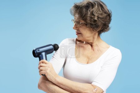 Foto de Retrato de atractiva mujer madura de pelo gris sosteniendo masajeador, tratamiento, de pie aislado sobre fondo azul. Concepto de salud - Imagen libre de derechos