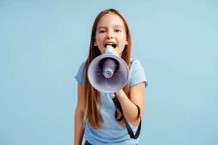 Porträt eines lächelnden schönen Mädchens in lässiger Kleidung, das einen Lautsprecher hält und etwas Isoliertes auf blauem Hintergrund ankündigt. Werbekonzept