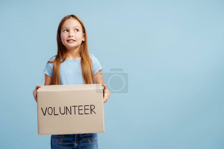Photo for Cute girl volunteer wearing casual clothes, holding cardboard box, isolated on blue background. Concept of support, help - Royalty Free Image