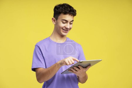 Foto de Muchacho sonriente retrato usando tableta digital, comunicación en línea aislada sobre fondo amarillo. Concepto tecnológico - Imagen libre de derechos