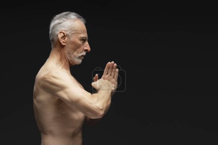 Foto de Retrato de vista lateral de un hombre serio y fuerte con el torso desnudo haciendo gestos, meditando, mirando hacia otro lado de pie aislado sobre fondo negro. Concepto de equilibrio - Imagen libre de derechos