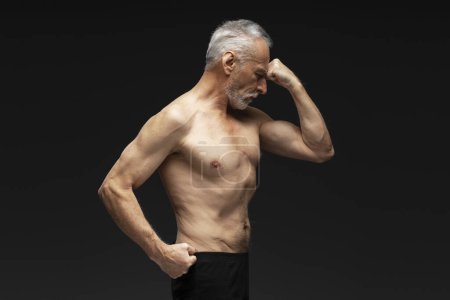 Téléchargez les photos : Portrait de séduisant homme âgé aux cheveux gris torse nu avec les yeux fermés debout isolé sur fond noir, gesticulant. Concept de mode de vie sain - en image libre de droit