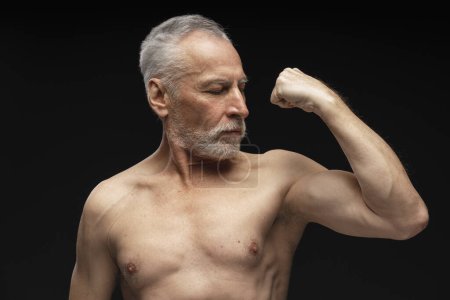 Téléchargez les photos : Portrait d'un séduisant homme âgé sérieux, athlète montrant des biceps, corps musculaire isolé sur fond noir. Concept de publicité - en image libre de droit