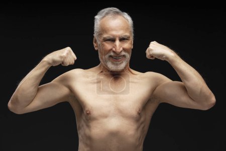 Photo for Portrait of smiling gray haired bearded man with naked torso showing biceps, muscular body looking at camera isolated on black background. Healthy lifestyle concept - Royalty Free Image