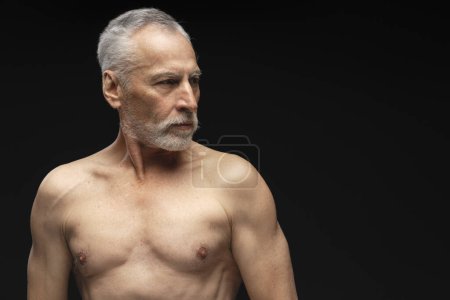 Téléchargez les photos : Portrait de sérieux cheveux gris, barbu, torse nu homme âgé regardant loin debout isolé sur l'espace de copie de fond noir. Concept de publicité - en image libre de droit