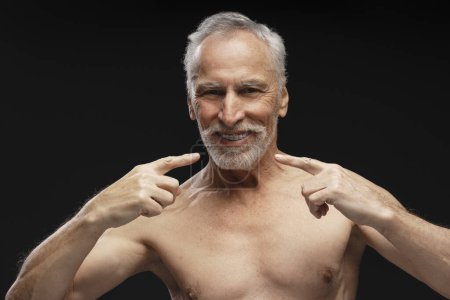 Photo for Portrait of smiling handsome gray haired man with naked torso pointing fingers at teeth, looking at camera isolated on black background. Dental care concept - Royalty Free Image