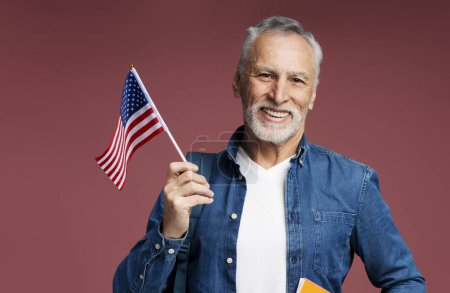 Foto de Retrato de un hombre mayor y guapo sonriente sosteniendo la bandera estadounidense celebrando el día de la Independencia aislado en el fondo. 4 de julio, concepto de libertad - Imagen libre de derechos
