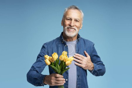 Photo for Portrait of handsome smiling senior man holding bunch of flowers isolated on blue background - Royalty Free Image