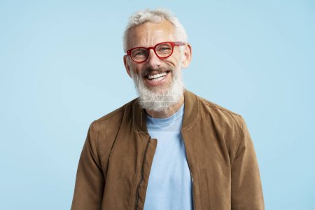 Téléchargez les photos : Portrait beau sourire 50 ans homme mûr avec des cheveux gris élégant portant des lunettes hipster rouge regardant la caméra isolée sur fond bleu. Concept de vision - en image libre de droit