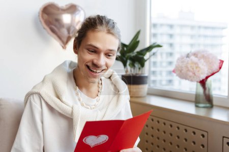 Téléchargez les photos : Portrait d'un homme souriant heureux tenant la lecture de la Saint-Valentin à sa petite amie alors qu'il était assis à la maison. Concept de rencontres, relations Saint-Valentin - en image libre de droit