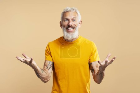 Téléchargez les photos : Portrait d'homme mûr souriant, hipster élégant avec cheveux gris et barbe gestuelle enregistrement vidéo regardant la caméra debout isolé sur fond beige. Communication en ligne - en image libre de droit