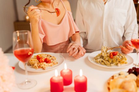 Photo for Couple holding hands, eating food sitting in modern restaurant with candles. Man and woman celebration Valentine's day. Date, love concept - Royalty Free Image