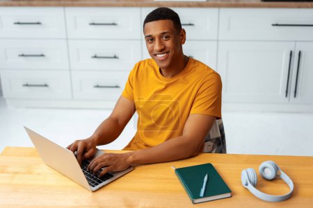 Photo for Portrait of handsome smiling African American man, freelancer, copywriter typing on keyboard wearing stylish yellow t shirt sitting on workplace, using laptop, remote job. Online education concept - Royalty Free Image