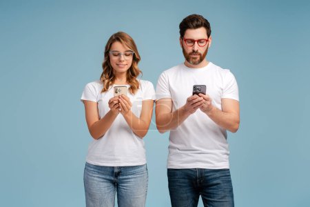 Photo for Smiling couple of friends holding mobile phones, communication online isolated on blue background. Technology, social media addiction concept - Royalty Free Image