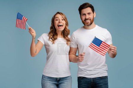 Téléchargez les photos : Heureux homme et femme tenant des drapeaux américains isolés sur fond bleu. Vote, Concept du jour d'élection - en image libre de droit
