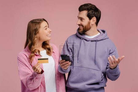 Photo for Happy smiling couple holding plastic credit card and mobile phone, isolated on pink background. Online shopping. Internet banking. Cashless payment. Paying bills. Booking and food ordering - Royalty Free Image