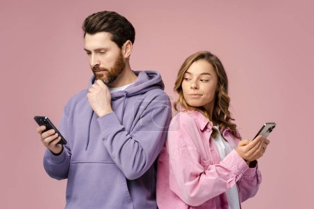 Photo for Interested woman looking at smartphone of her bearded boyfriend isolated on pink background. Happy friends holding mobile phones, communication online. Technology, social media addiction concept - Royalty Free Image