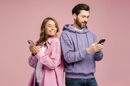 Photo for Smiling woman looking at smartphone of her bearded boyfriend isolated on pink background. Happy friends holding mobile phones, communication online. Technology, social media addiction concept - Royalty Free Image