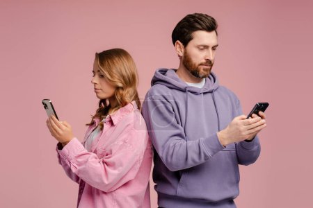 Photo for Couple of serious friends holding mobile phones, communication online isolated on pink background. Technology, social media addiction concept - Royalty Free Image